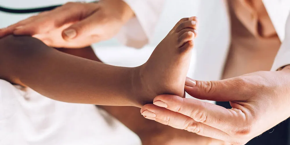 Close-up of a pediatrician examining a child’s leg and foot.