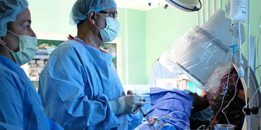 An interventional cardiologist performs a heart procedure while surrounded by other physicians and staff.