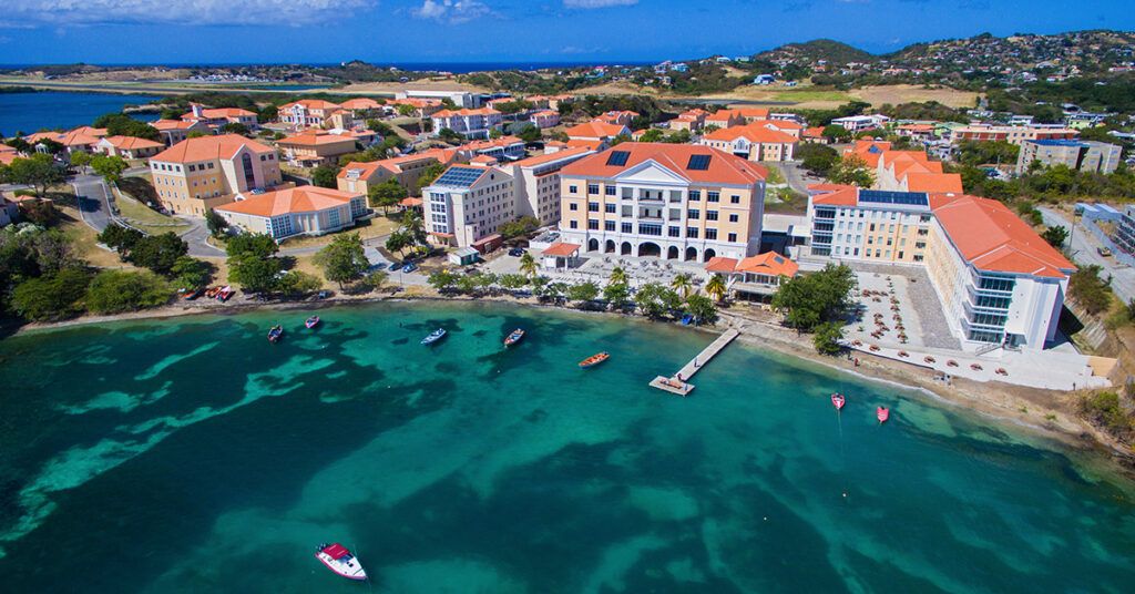 Aerial view of the St. George's University (SGU) campus in Grenada, showing buildings along the turquoise Caribbean Sea coastline.