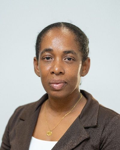Black woman with hair pulled back, wearing a brown blazer and gold necklace against a neutral background