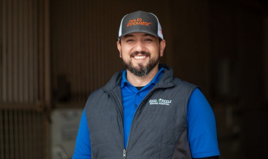 Dr. Heath Soignier, SGU DVM '12 alumnus and Equine Veterinarian, wearing scrubs while examining a horse in a stable.