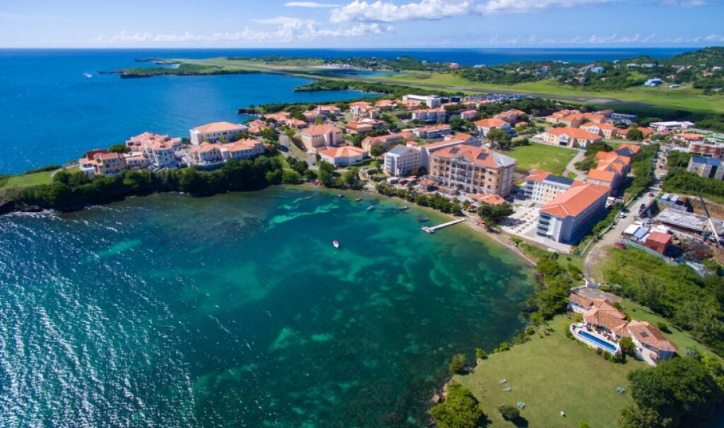 Panoramic view of the Caribbean island of Grenada, featuring lush green hills, turquoise water, and tropical coastline.