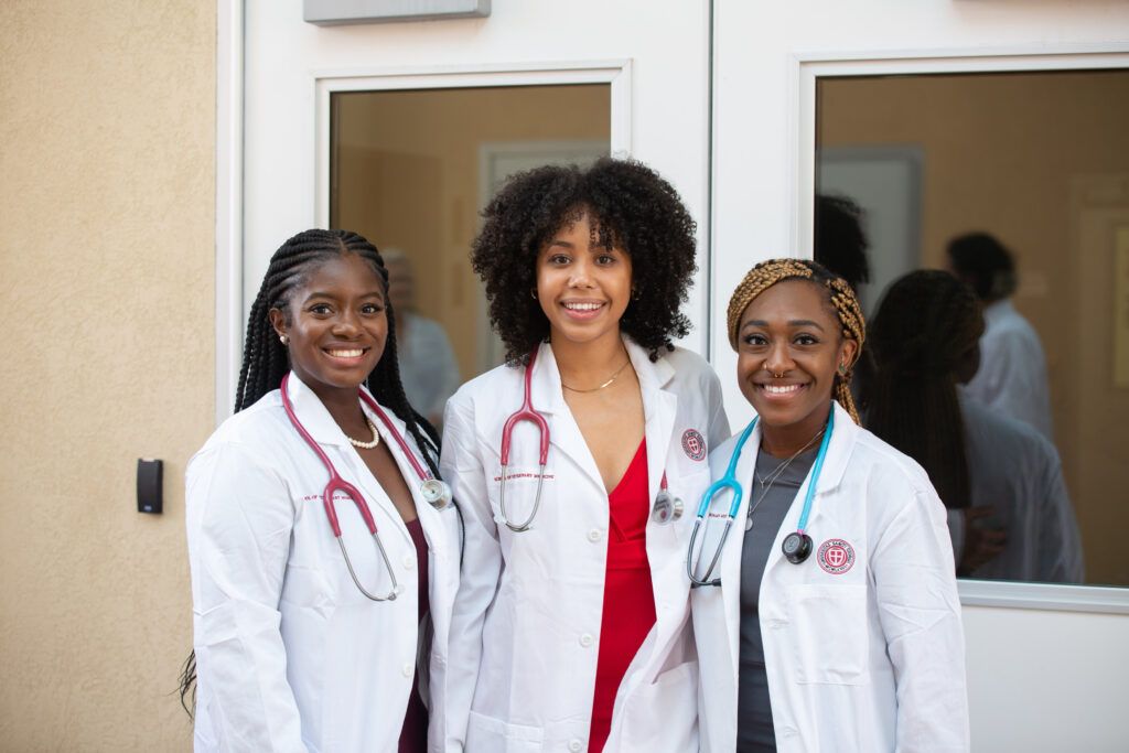Group of 3 SGU students standing together posing for a picture in their white coats.