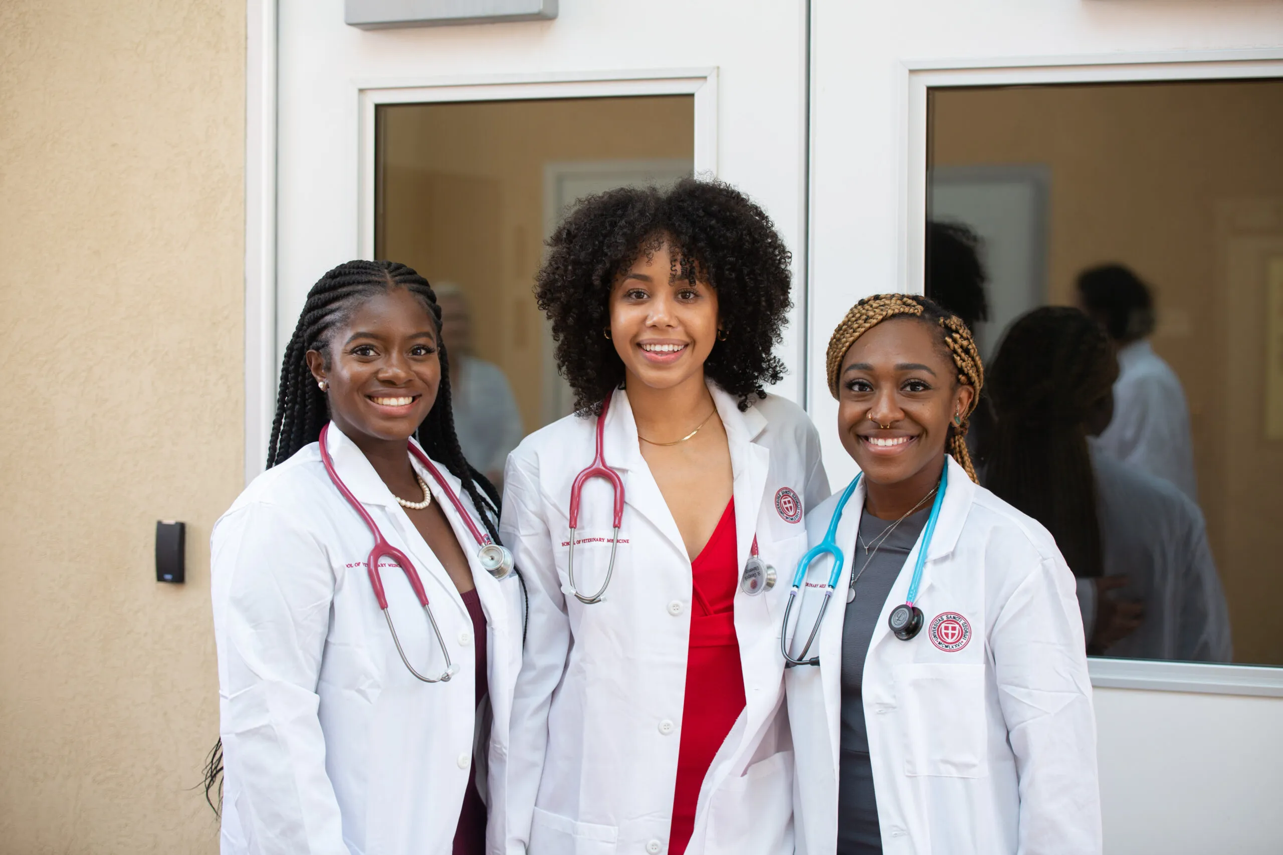 Group of 3 SGU students standing together posing for a picture in their white coats.