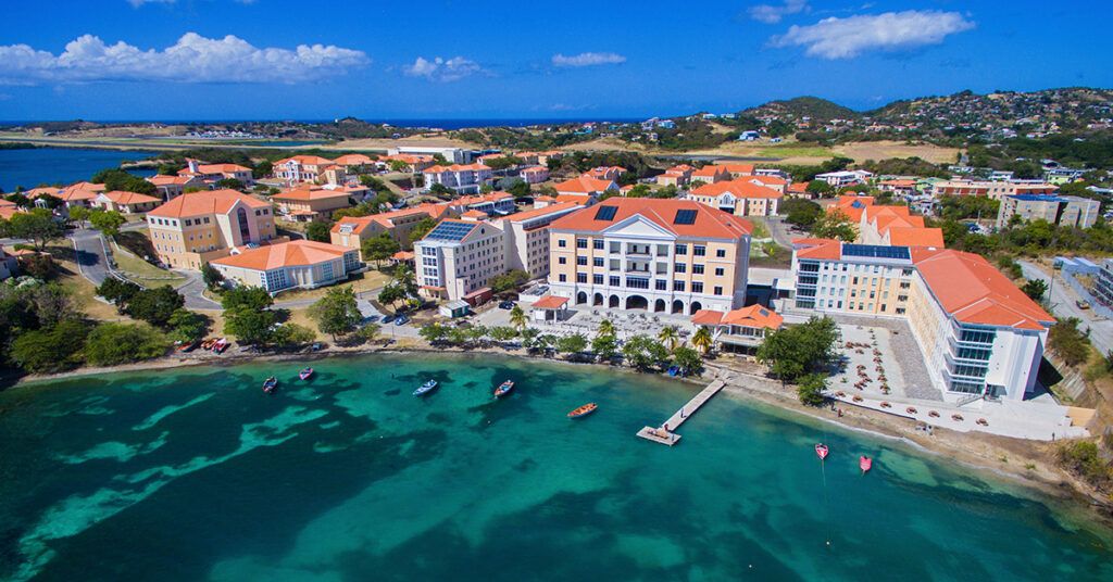 Aerial view of the SGU True Blue campus in Grenada, showcasing university buildings and the pier on the turquoise Caribbean Sea.