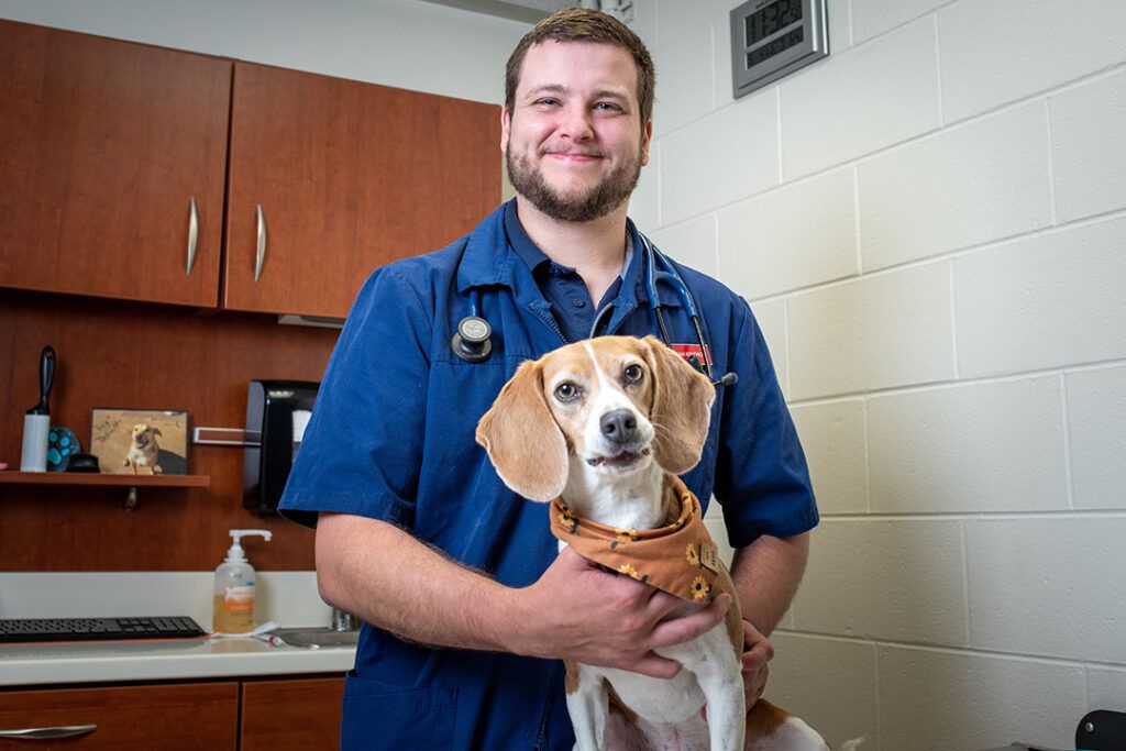 An SGU graduate in blue lab gown smiling and holding an adorable puppy.