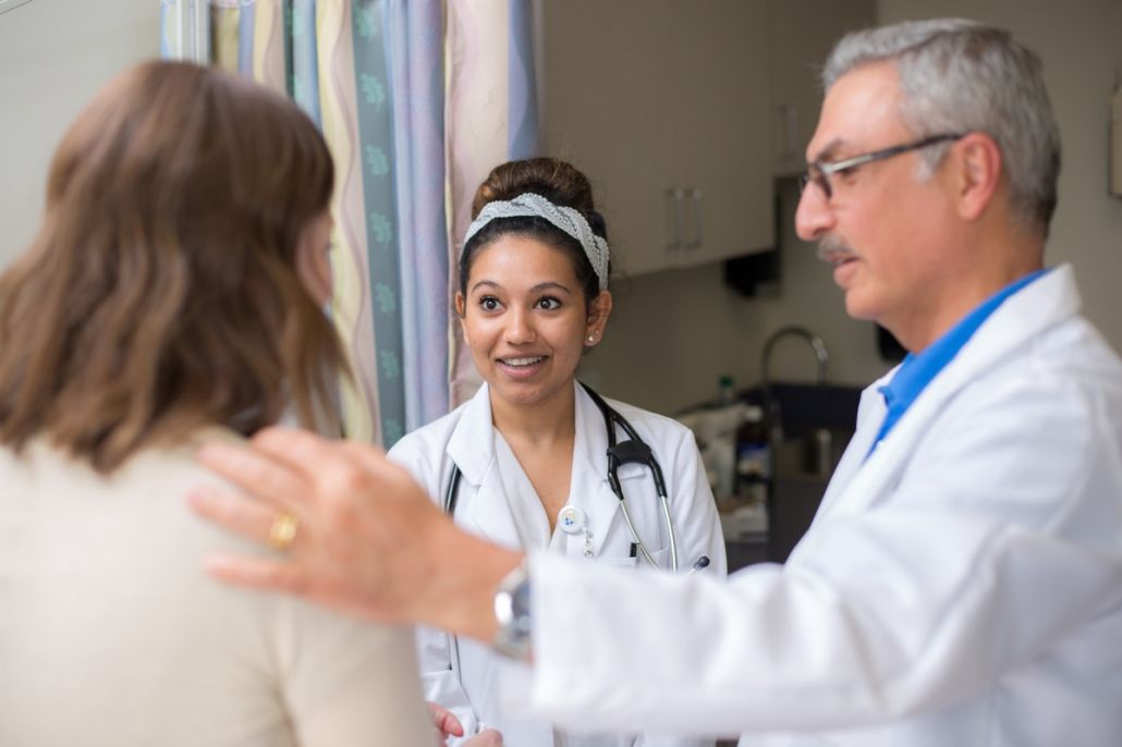 Female medical student on a clinical rotation observing a senior physician consulting with a female patient in an examination room. News