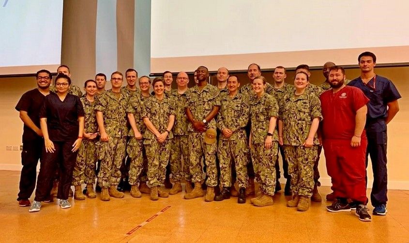 Large group of U.S. military personnel in Navy camouflage uniforms posing with medical students, related to the USNS Comfort mission. News
