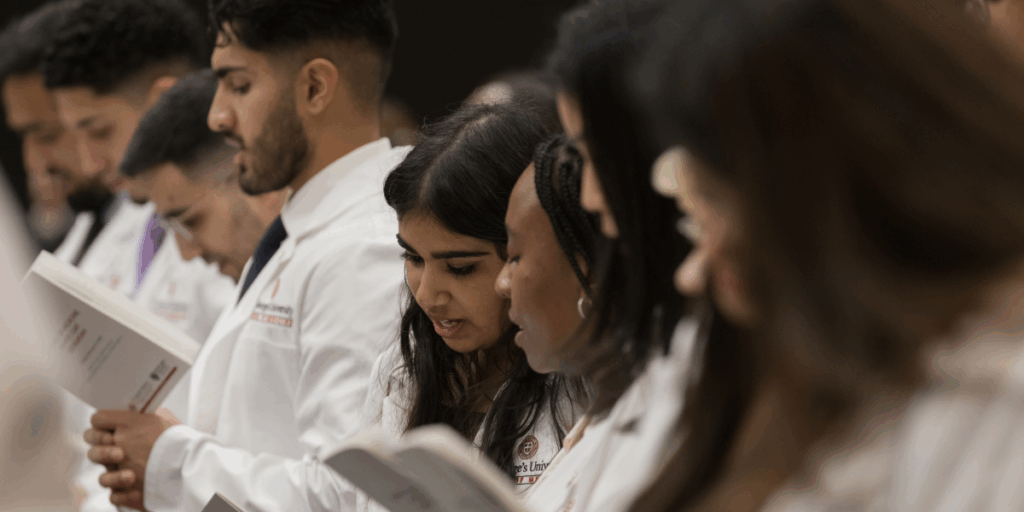 Group of SGU students in their white coats reading from book