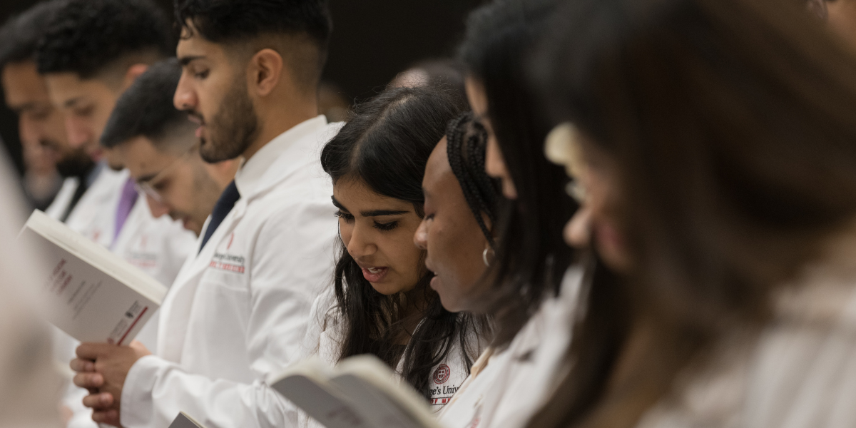 Group of SGU students in their white coats reading from book